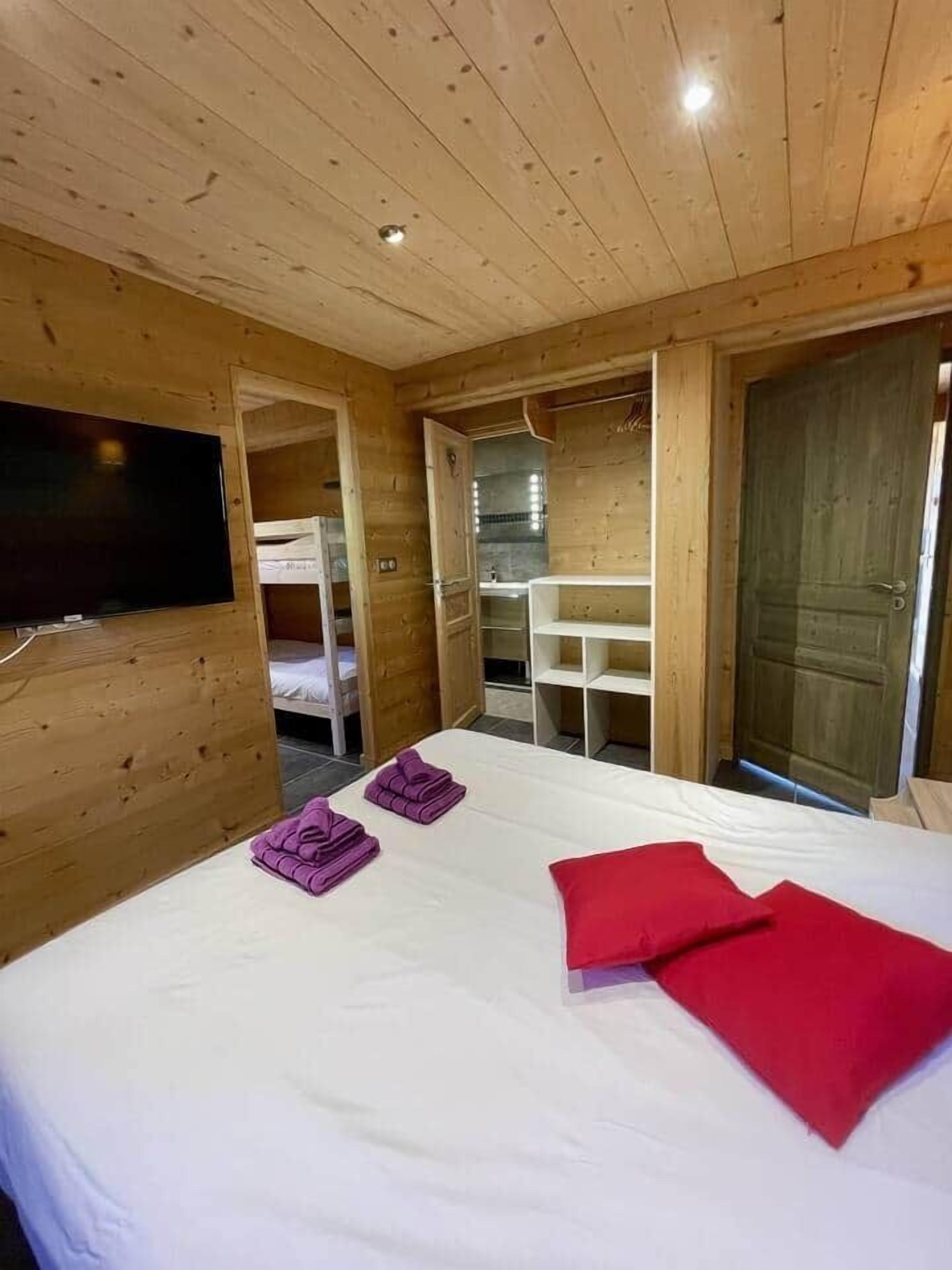 A wooden cabin room with a bed, a TV, and a bunk bed in the background.