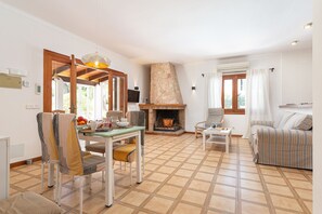 Ein Wohnzimmer mit Kamin, Esstisch, Stühlen, einer Couch und einem Fernseher.