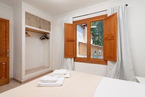 Ein Schlafzimmer mit einem Bett, einem Holzschrank, einem Fenster mit Vorhängen und einem Handtuch auf dem Bett.