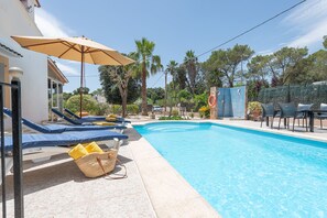 Ein Swimmingpool mit Liegestühlen und Sonnenschirm, umgeben von Palmen und einem Zaun.