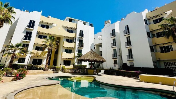 A resort with a swimming pool, palm trees, and multi-story buildings. - Beautiful apartment with the best location in cabo san lucas 8 min from the beach (Cabo San Lucas)