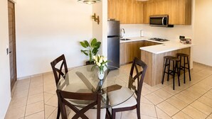 A modern kitchen with wooden cabinets, a stainless steel refrigerator, a microwave, and a gas stove. There is a glass dining table with chairs and a vase with flowers. - Beautiful apartment with the best location in cabo san lucas 8 min from the beach (Cabo San Lucas)