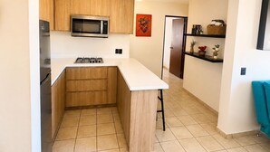 A compact kitchen with wooden cabinets, a microwave, a stove, and a small island. - Beautiful apartment with the best location in cabo san lucas 8 min from the beach (Cabo San Lucas)