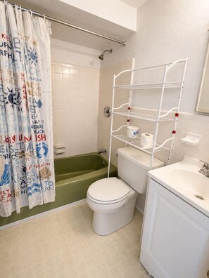 Kylpyhuone, jossa on suihku, wc ja valkoiset hyllyt.
