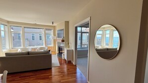 Ett rymligt vardagsrum med en soffa, en TV och stora fönster med utsikt över staden.