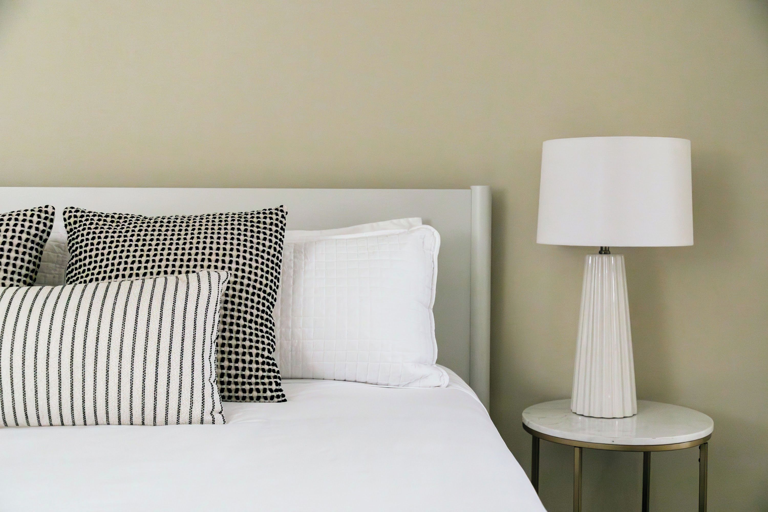 A bed with white bedding, two patterned pillows, and a white lamp on a small table beside it.