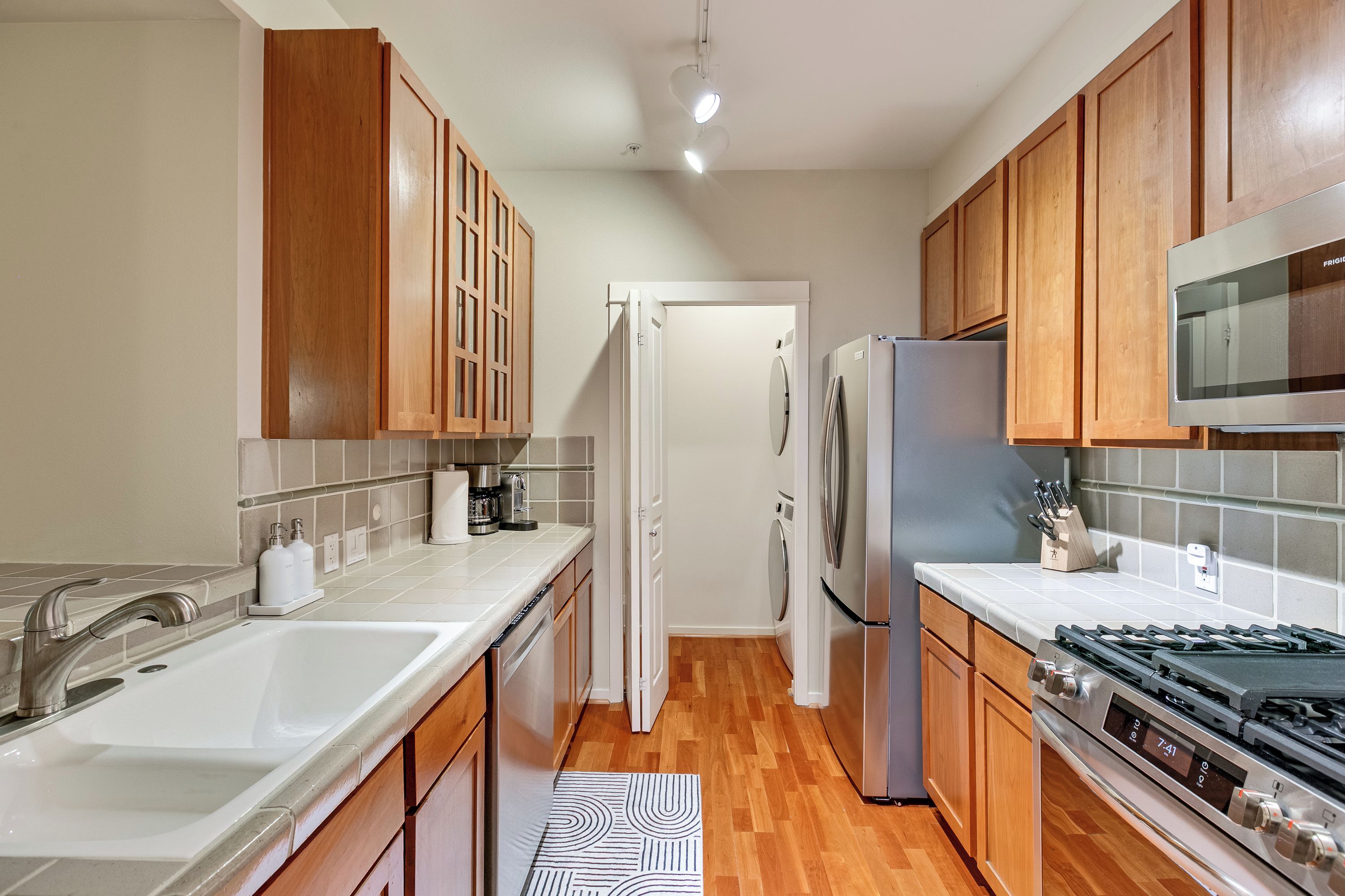 A compact kitchen with wooden cabinets, a stainless steel refrigerator, a microwave, and a stove.