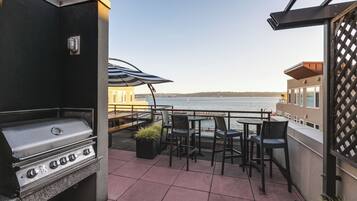 A patio with a grill, outdoor seating, and a view of the water.