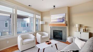 A modern living room with a fireplace, two white armchairs, a coffee table, and a sofa.