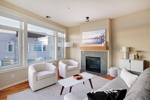 Un salon moderne avec une cheminée, deux fauteuils blancs, une table basse et un canapé.