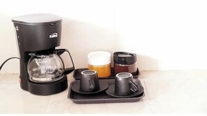 A coffee maker with a glass carafe, two black mugs, a small container with a lid, and a tray with two black cups. - Apartment a few steps from the main square  (Villa de Leyva)