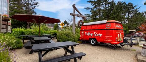 A red food truck with 'Village Scoop' branding parked near picnic tables and an umbrella.