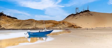 Ein Boot an einem sandigen Strand mit blauem Himmel und Hügeln im Hintergrund.