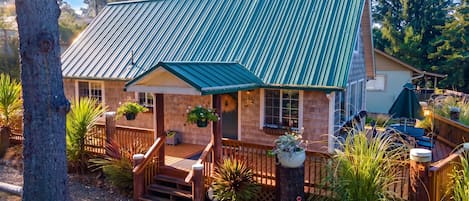 A house with a green metal roof, wooden deck, and a covered porch with potted plants.