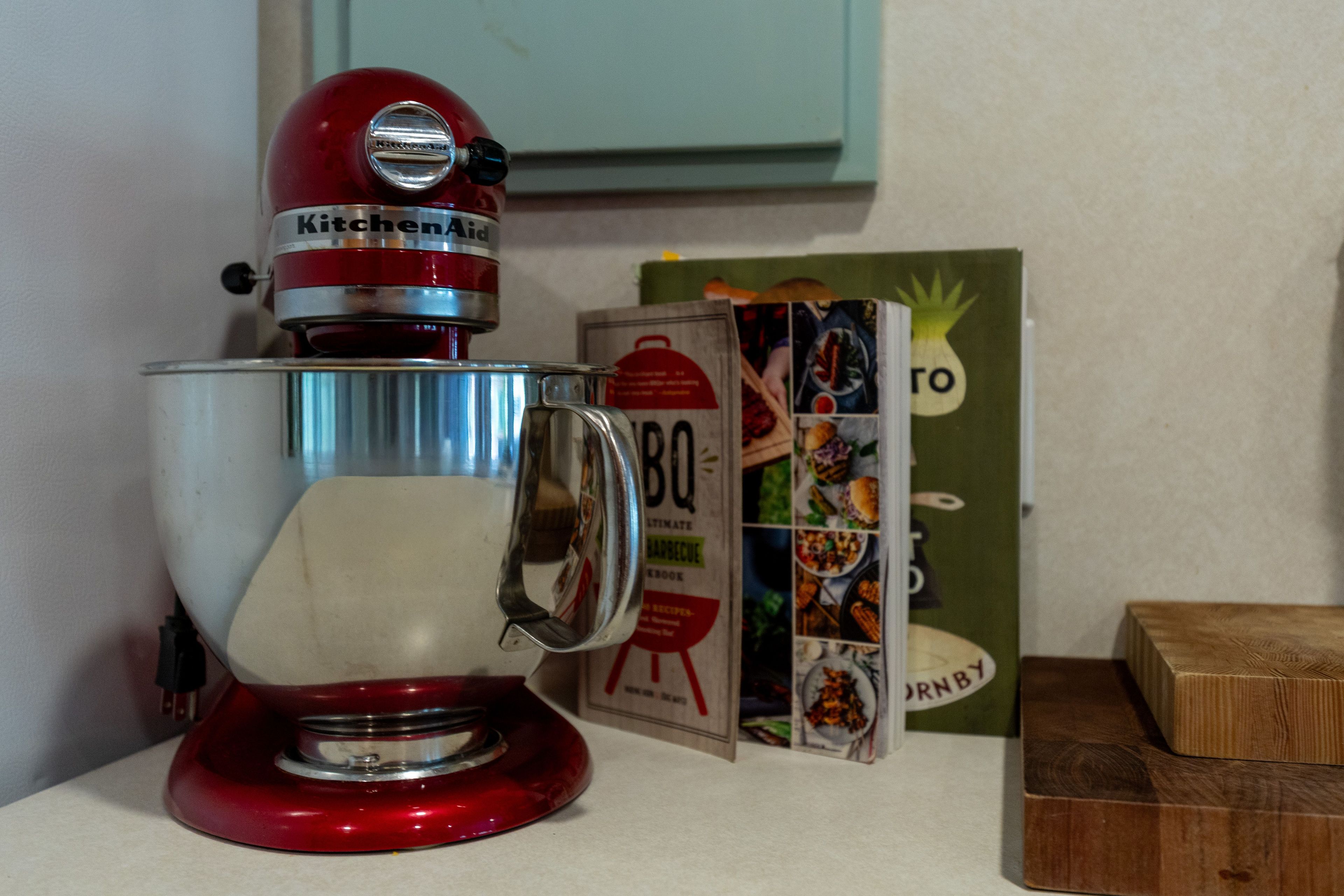 A red KitchenAid mixer on a kitchen counter with a cookbook and a wooden cutting board nearby.