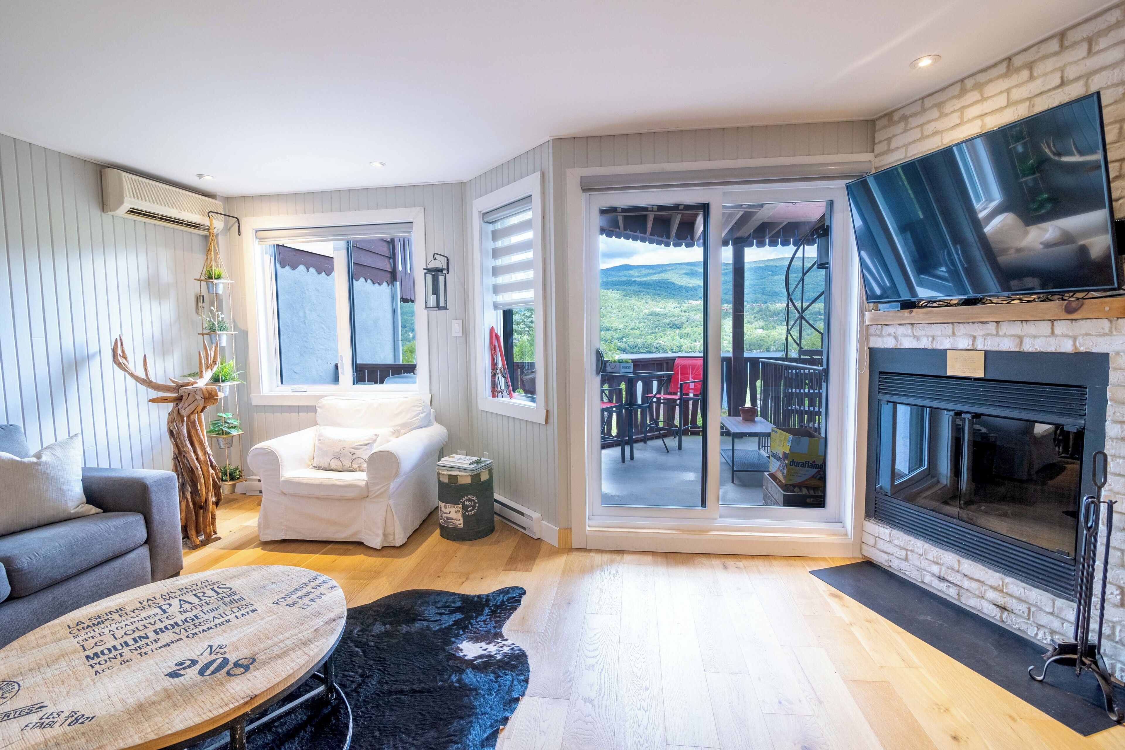 A living room with a fireplace, a sofa, a coffee table, and a view through the glass doors.