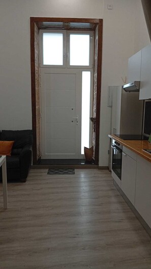 A compact living space with a kitchenette, a door with frosted glass panels, a black sofa, and a patterned rug. - Casa San Gregorio in the historic center of Telde, Las Palmas, Gran Canaria. (Telde)