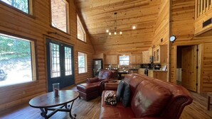 A log cabin interior with a leather sofa, a round table, and a kitchen area. - Private Cabin Retreat w/Hot Tub, Fire Pit & Loft (Broken Bow)