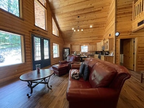 Ein Holzblockhaus-Interieur mit Ledersofa, rundem Tisch und Küchenzeile.