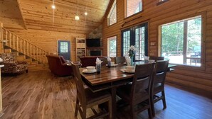 A wooden interior with a dining table, chairs, a staircase, and large windows. - Private Cabin Retreat w/Hot Tub, Fire Pit & Loft (Broken Bow)