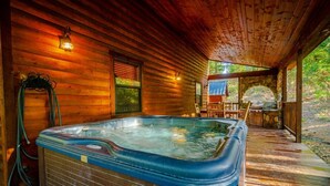 A wooden cabin with a hot tub, a stone archway, and a covered porch. - Private Cabin Retreat w/Hot Tub, Fire Pit & Loft (Broken Bow)