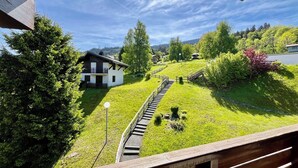 Een huis met twee verdiepingen en een balkon, omringd door weelderige begroeiing en een heldere lucht.