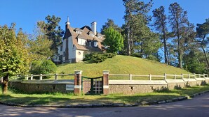Een groot huis op een heuvel, met een stenen muur en poort, omringd door bomen.