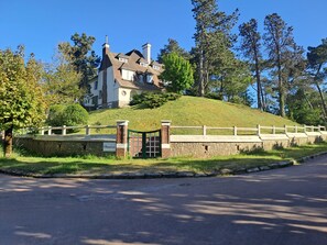 Ein großes Haus auf einem Hügel mit einer Steinmauer und einem Tor, umgeben von Bäumen.