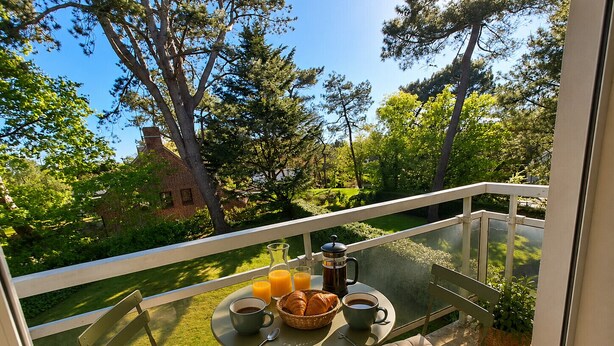 Een balkon met een ontbijtje gedekt, inclusief croissants, koffie en sap.