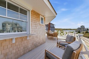 A wooden deck with outdoor furniture, a view of a lake, and a house in the background.