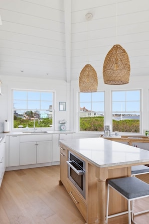 A modern kitchen with a large island, white cabinetry, and a view of the sea.
