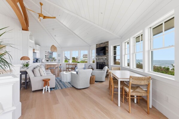 A spacious living area with a fireplace, dining table, and large windows overlooking the ocean.