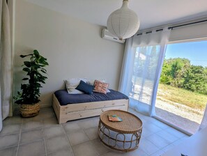 Ein Zimmer mit einem Bett, einem runden Korbtisch, einer Topfpflanze und einem großen Fenster.