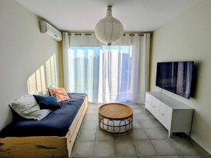 Ein Zimmer mit einem Bett, einem Fernseher, einem Korbsessel und einem großen Fenster mit Vorhängen.