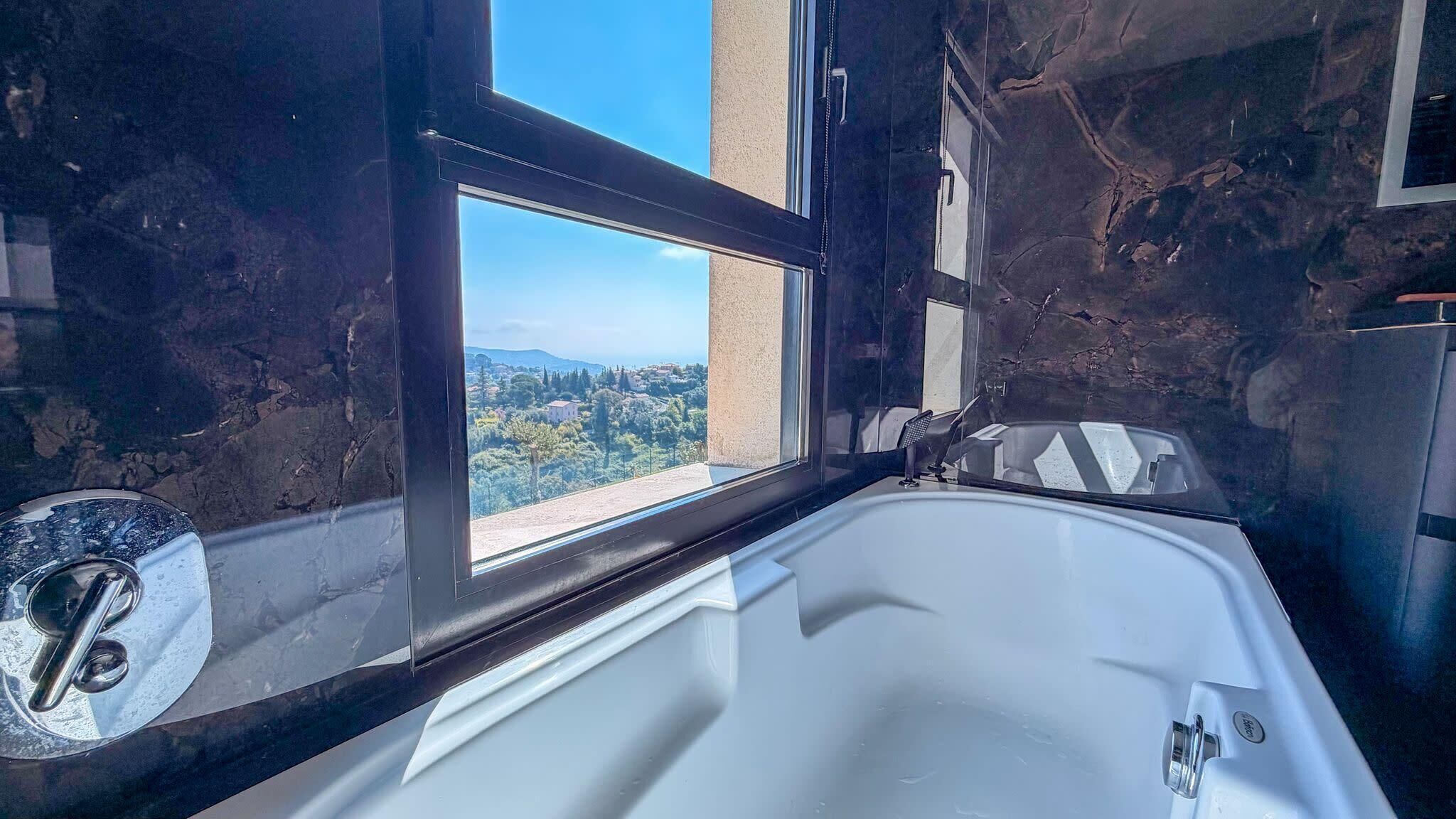 Une salle de bain dotée d’une grande baignoire, d’une fenêtre offrant une vue sur le paysage urbain et d’un mur en marbre.