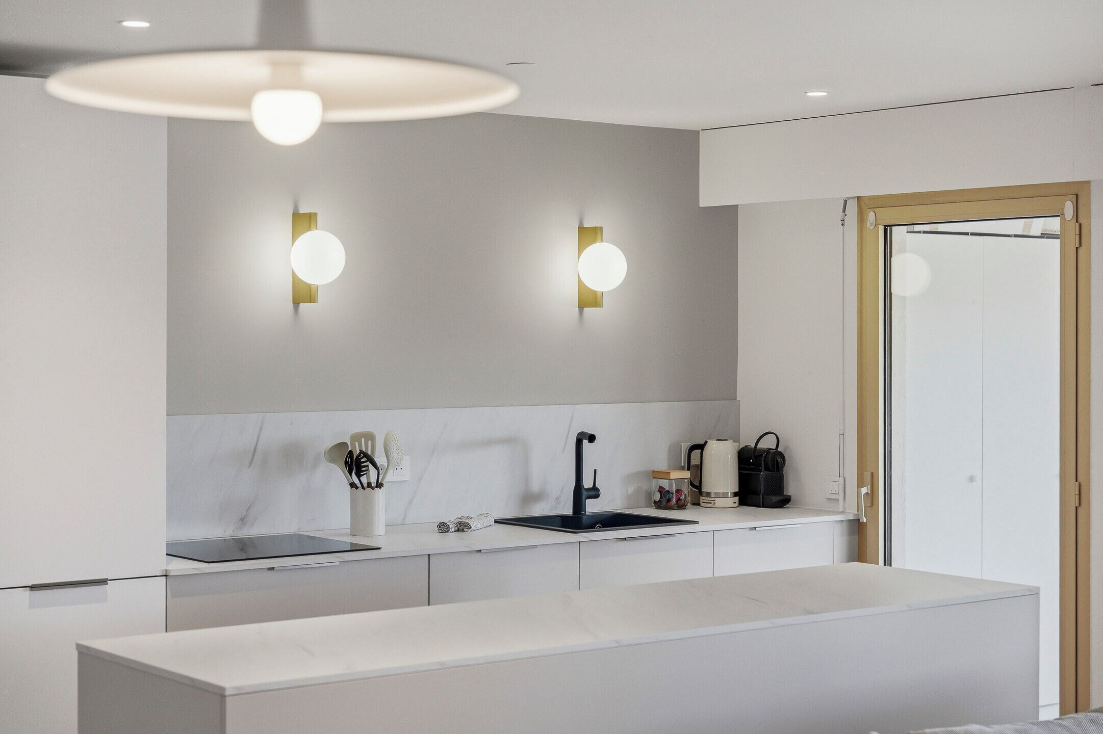 A modern kitchen with a white countertop, black faucet, and two wall-mounted lights.