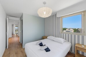 Une chambre d’hôtel comprenant un lit, une table de chevet, une commode, une fenêtre donnant sur un paysage agréable et un couloir menant à une autre pièce.