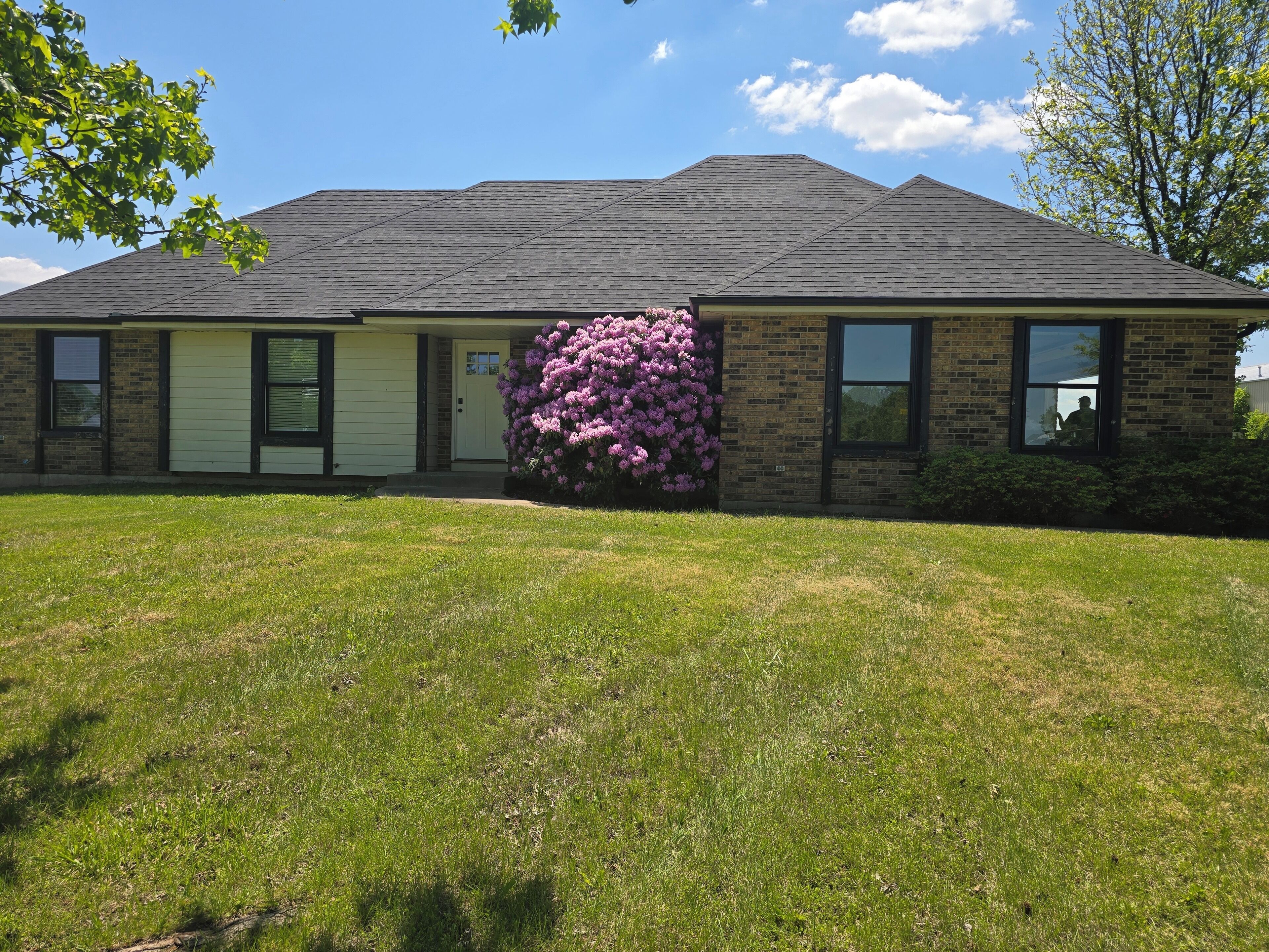 A two-story house with a brick facade, a front lawn, and a large bush with purple flowers.
