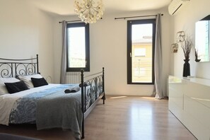 Ein Schlafzimmer mit einem Bett, einem Schminktisch, zwei Fenstern und einer Deckenleuchte.