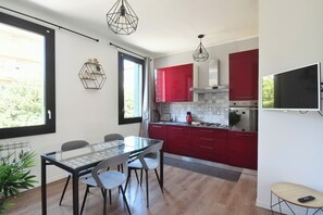 A modern kitchen with red cabinets, a glass dining table, and pendant lights. - Corte Casati - Stylish, Cozy, New, Free Parking (Venezia)