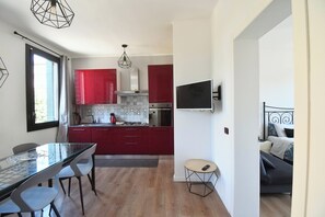 A modern kitchen with red cabinets, a dining table with chairs, a small round table with a chair, and a TV mounted on the wall. - Corte Casati - Stylish, Cozy, New, Free Parking (Venezia)