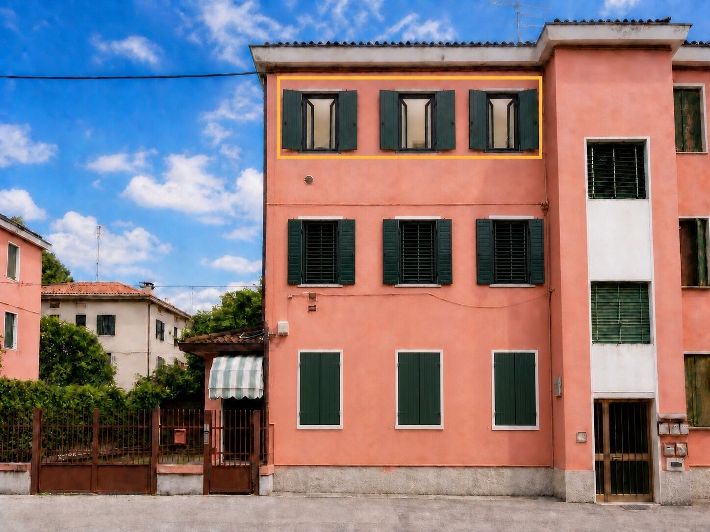 A pink building with green shutters and a gated entrance.