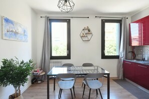 Ein Essbereich mit einem Glastisch und Stühlen, einer roten Küche und einem großen Fenster.