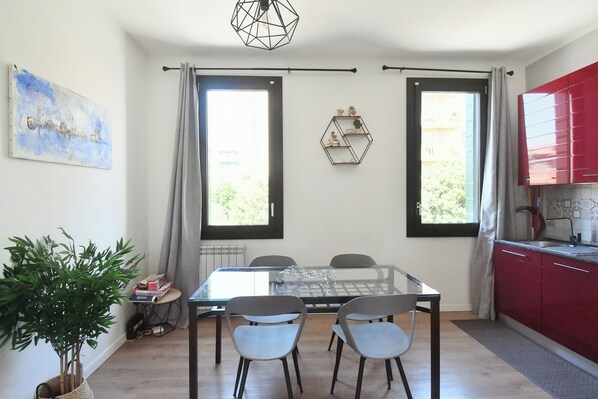 A dining area with a glass table and chairs, a red kitchen, and a large window. - Corte Casati - Stylish, Cozy, New, Free Parking (Venezia)