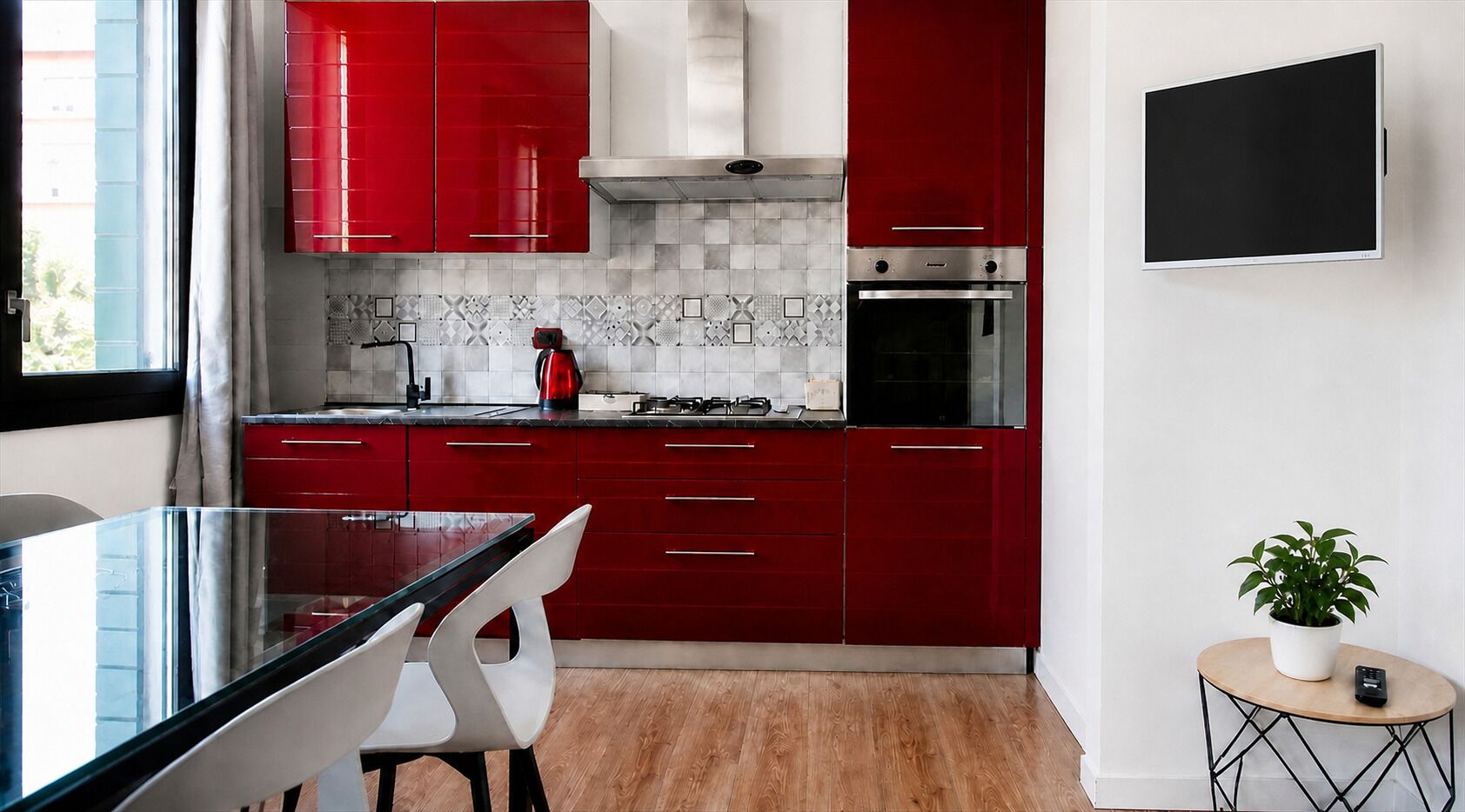A modern kitchen with red cabinets, a stainless steel range hood, and a built-in oven.