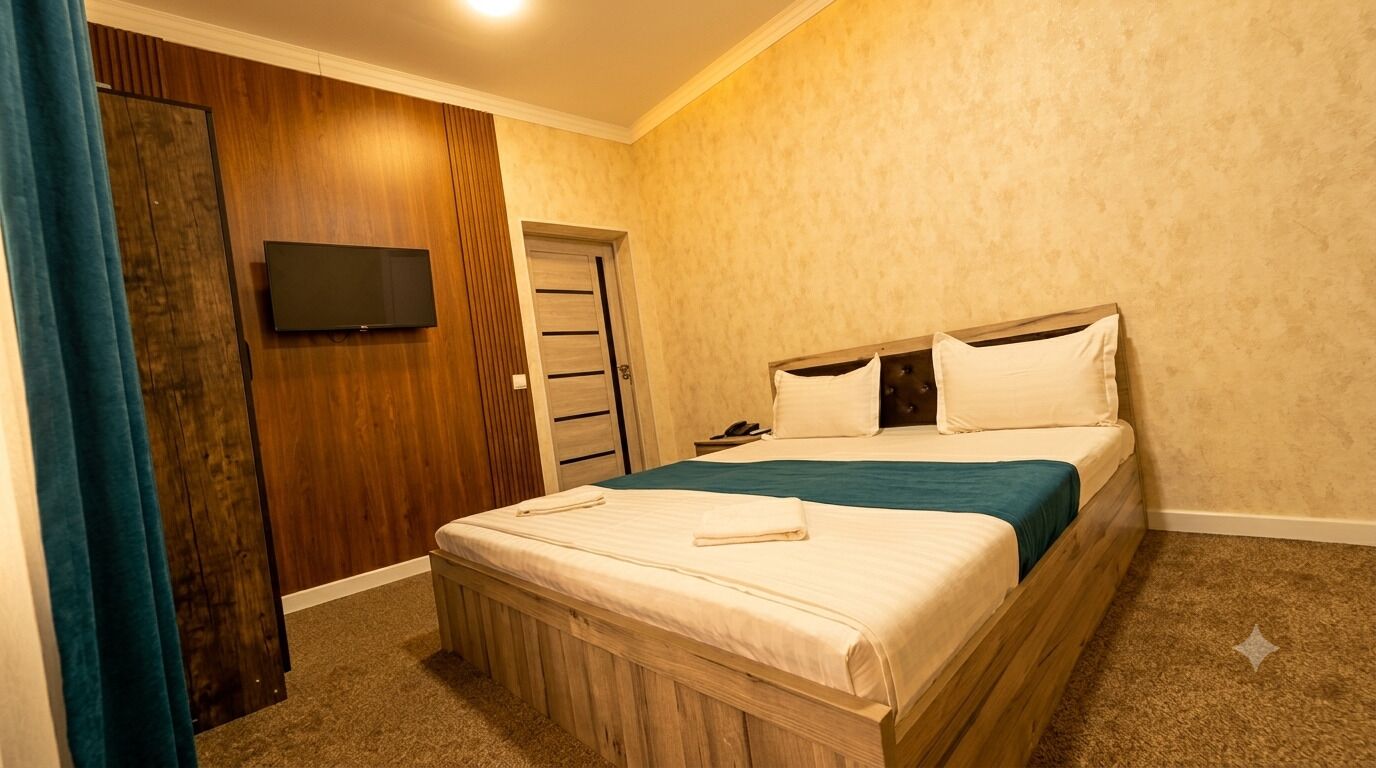 A bedroom with a bed, a television mounted on the wall, and a wooden wardrobe.
