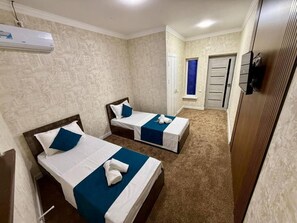 A hotel room with two beds, a wardrobe, a window with blue curtains, and an air conditioning unit. - Usmoon Hotel (Tashkent)