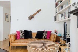 A living room with a sofa, ottoman, and a wall-mounted guitar. - Charming 1BDR Retreat with Garden in West London (London)