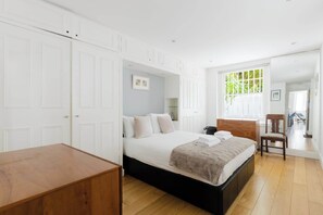 A bedroom with a bed, wooden floor, white wardrobe, and a window with a view. - Charming 1BDR Retreat with Garden in West London (London)
