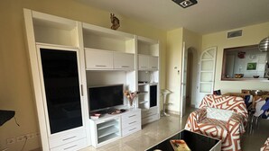 Ein Wohnzimmer mit Fernseher, weißen Schränken, einer Couch und einem Couchtisch.